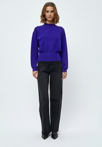 Maglione lavorato a maglia viola con scollo tondo, polsini e orlo a coste, abbinato a jeans neri a vita alta con gamba larga e scarpe nere a punta.