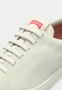 Λευκό αθλητικό παπούτσι με υφή στο επάνω μέρος, γκρι κορδόνια και κόκκινο λογότυπο "CAMPER" στη γλώσσα. Λείο πέλμα και μινιμαλιστικός σχεδιασμός.