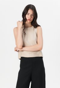 Beige zkrácený top bez rukávů s kulatým výstřihem a texturovaným materiálem, kombinovaný s černými kalhotami s vysokým pasem. Jednoduchý a minimalistický design.