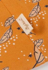 Cotton fabric in orange with a leaf and dot pattern. Includes a cream label with black text. Soft texture, rectangular shape.