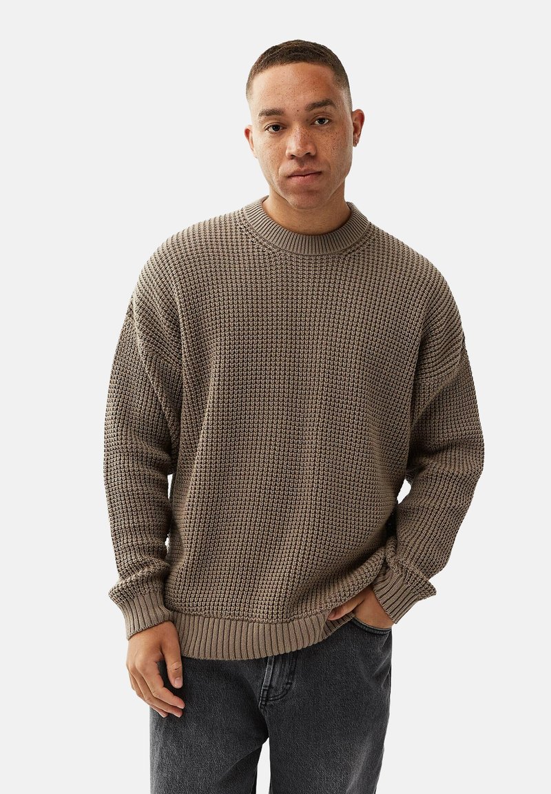 Kraftig strikket sweater i taupe med en rund halsudskæring samt ribbede manchetter og kant. Stoffet har et struktureret mønster og en løs pasform.