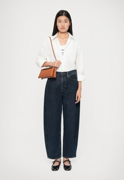 Hvid skjorte med knapper, mørkeblå vide jeans, sorte flade sko og en brun crossbody taske. Outfittet har enkle linjer og klassiske farver.