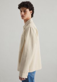 Beige overhemden van katoen met een borstzak, lange mouwen en een relaxte pasvorm, gecombineerd met blauwe denim jeans.