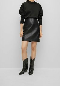 Mini gonna nera in pelle con bottoni laterali, abbinata a un maglione textured nero e stivali da cowboy neri con punta affusolata.