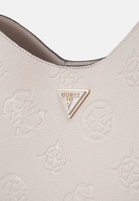 Borsa color crema con una morbida texture in pelle, caratterizzata da motivi in rilievo e un accento metallico a forma triangolare.