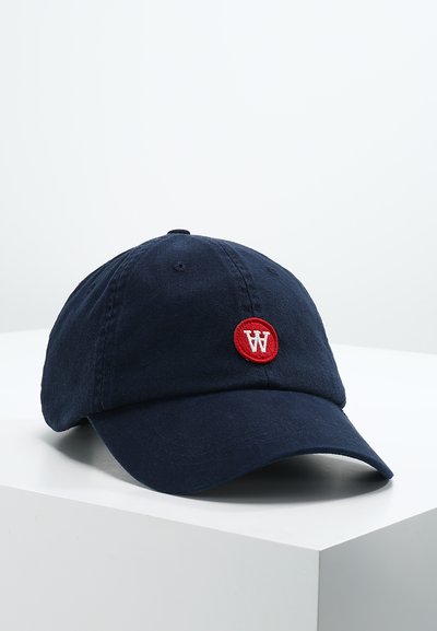 Tumši zila kokvilnas beisbola cepure ar apaļu sarkanu uzlīmi, uz kuras ir balta "W" logo, izliekta viziera un regulējama siksna aizmugurē.
