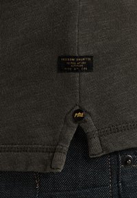 Donkergrijs, gestructureerd stoffen shirt met een label waarop "Freedom Unlimited" staat, voorzien van een zwarte knop met gouden accenten op de zijnnaad.