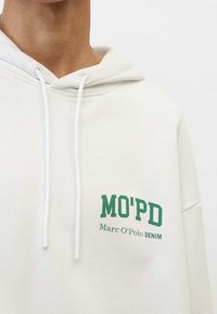 Sudadera con capucha blanca hecha de tela suave con un estampado verde que dice "MO'PD" y "Marc O'Polo DENIM", con capucha ajustable mediante cordón y bolsillo canguro.