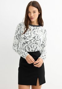 Suéter esponjoso de patrón blanco y negro con manga larga, escote redondo y acabado texturizado, combinado con una falda negra con una abertura lateral.