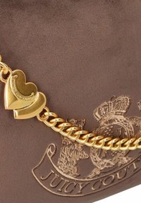 Braune Wildleder-Handtasche mit goldfarbenen Beschlägen; verfügt über einen herzförmigen Anhänger und ein geprägtes Logo mit Kronendetails.