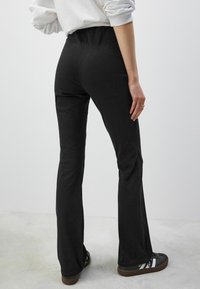Zwarte flared broeken met een elastische tailleband, gemaakt van een soepele, rekbare stof. Bevat casual schoenen met een bruine zool en witte accenten.