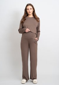 Bruine lange mouwtop en bijpassende taps toelopende broek, gemaakt van zachte stof met een gladde textuur. De top heeft een cropped ontwerp en zakken in de taille.