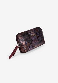 Cartera con estampado floral en tonos púrpura oscuro y cobre, hecha de cuero texturizado, con cierre de cremallera y correa para la muñeca.