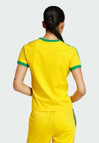 Żółta koszula z krótkim rękawem z zielonym obszyciem, wykonana z miękkiego materiału. Projekt obejmuje klasyczny okrągły dekolt i dopasowany krój.