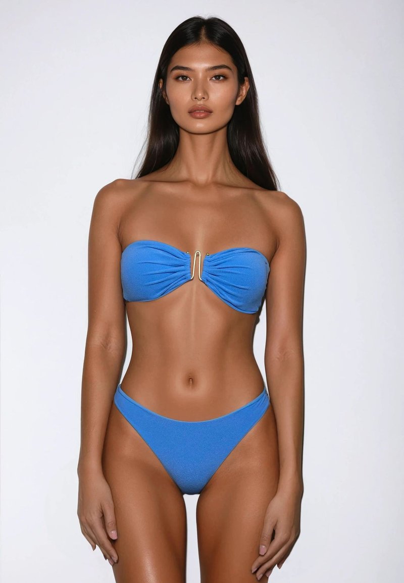 Blauwe bandeau-bikini met geplooide stof en gouden hardware detail in het midden, gecombineerd met high-waisted onderstukken. Zachte textuur.