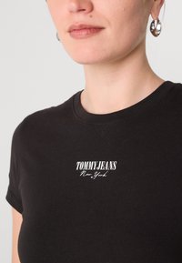 Černé bavlněné tričko s přiléhavým st�řihem a kulatým výstřihem. Na hrudi je bílé logo "TOMMY JEANS New York" v tučném písmu.