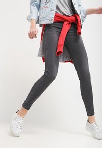 Grå smala jeans med en slät yta, som har en medelhög midja och subtila blekningar. Kombinerat med vita mönstrade sneakers och en röd sweatshirt knuten i midjan.