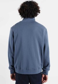 Sweat-shirt bleu avec un col haut, une texture douce et des manches longues. Présente un petit logo sur l'épaule gauche et un ourlet côtelé.