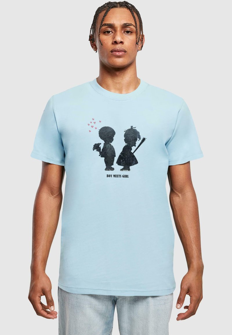 Lyseblå t-shirt med et grafisk motiv af to silhuetter, en dreng og en pige, med hjerter over og tekst "BOY MEETS GIRL" nedenfor. Glat stof.