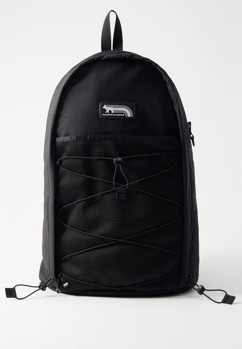 Sac à dos noir avec un dessus arrondi, poches avant en maille, cordon élastique, et écusson logo. Tissu léger avec une texture lisse.