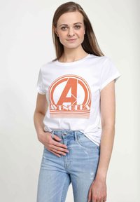 Biała bawełniana koszulka z pomarańczowym logo "Avengers" w okrągłym kształcie. Połączona z jasnoniebieskimi dżinsami. Gładka tekstura, krótkie rękawy.