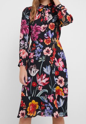 Schwarzes knielanges Kleid mit langen Ärmeln, lebhaften, mehrfarbigen großen Blumenmustern und einer kleinen Schleife am Ausschnitt.