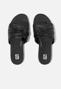 Zwarte leren slipper-sandalen met een gedraaide riemontwerp, platte zool en een logo op de voetbed, wat zorgt voor een stijlvolle en moderne uitstraling.