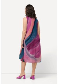 Vestido sin mangas con pliegues en vibrantes tonos de rosa, azul y verde con un diseño fluido. Combinado con sandalias de tacón cuadrado rosas.