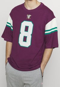 Camiseta violeta de manga corta con el gran número blanco 8, detalles en color azul verdoso y un logo con tema de hockey en el pecho. Material de algodón cómodo.