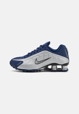 Chaussure de sport pour homme en bleu marine et argent avec logo Nike, dotée d'un amorti ressort sous la semelle et d’une fermeture à lacets.