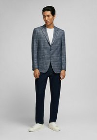 Gestructureerde blauwe geruite blazer met geknipte revers, gedragen over een wit t-shirt, gecombineerd met donkerdenim broek en witte sneakers.