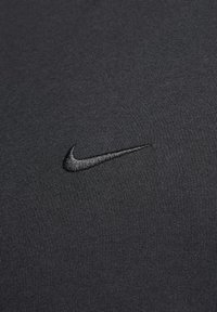 Black athletic shirt with a textured fabric, featuring a black embroidered Nike swoosh logo on the left chest area.