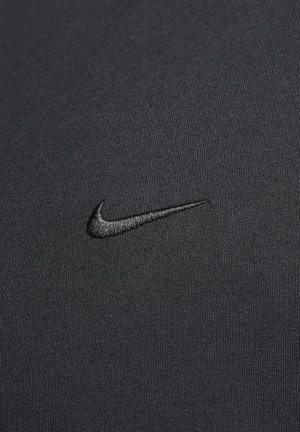 Black athletic shirt with a textured fabric, featuring a black embroidered Nike swoosh logo on the left chest area.
