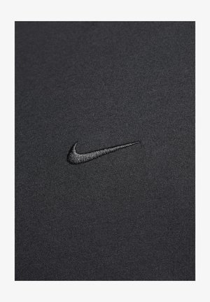 Tricou sport negru dintr-un material texturat, având un logo Nike brodat în negru pe partea stângă a pieptului.