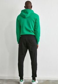 Grön huvtröja, svarta avsmalnande joggers och vita sneakers med gröna detaljer. Huvtröjan har en söm på baksidan; joggers har en bakficka.