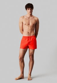 Pantaloni da bagno rossi con vita elastica e coulisse, caratterizzati da un taglio a metà coscia e da un tessuto liscio e leggero.