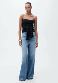 Top nero senza spalline con texture arricciata e nodo laterale, abbinato a jeans in denim azzurro chiaro con gamba ampia, caratterizzati da un lavaggio sbiadito e orlo risvoltato.