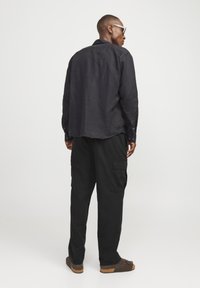 Camisa de lino negra con un corte relajado, mangas largas y detalles de botones, combinada con pantalones cargo negros holgados y calzado marrón.