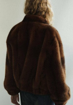 Veste en fausse fourrure marron avec un col haut, coupe oversize et texture douce. Le design en forme de V à l'arrière ajoute de l'intérêt visuel.