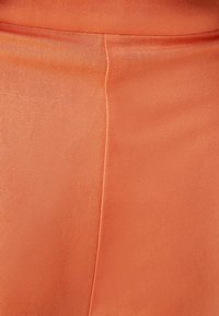 Tela naranja con una textura suave, con un brillo sutil. La imagen en primer plano muestra una costura precisa y un color sólido sin patrones.