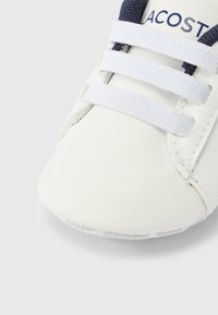 Λευκός δερμάτινος αθλητικός παπούτσι με ναυτικές λεπτομέρειες, διαθέτει τρεις ελαστικές κορδονιών, στρογγυλεμένη μύτη και ραμμένο σχέδιο γύρω από τη σόλα.