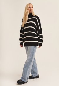 Black and white striped knit sweater with a high neckline and oversized fit, paired with light blue denim flared jeans and black platform shoes.