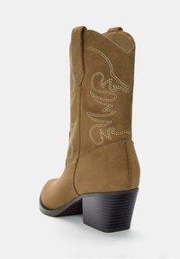Botine western din suede maro, cu toc negru stratificat. Prezintă cusături decorative albe într-un model spiralat. Design cu vârf rotund.