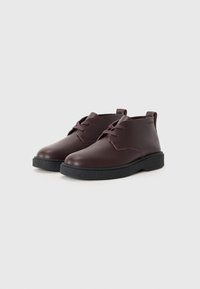 Scarpe in pelle marrone con finitura liscia, design con lacci, punta arrotondata e suola in gomma nera texturizzata.