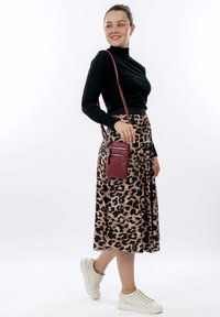 Sort ribbet turtleneck, leopardmønstret midi-nederdel, vinrød crossbody taske og hvide sneakers. Modellen står foran en neutral baggrund.