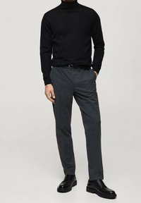 Černý rolák, šedé na míru šité kalhoty a černé šněrovací boty. Hladká textura a přiléhavý střih. Minimalistický styl bez vzorů.