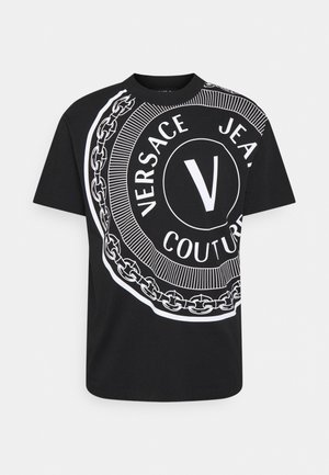 T-shirt noir à manches courtes avec un grand logo circulaire blanc affichant "Versace Jeans Couture" et un graphisme de chaîne sur le devant.