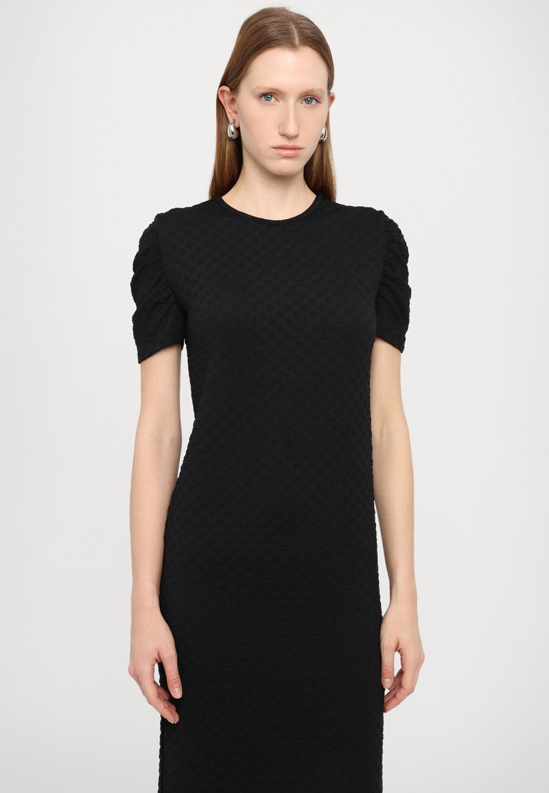 Vestido negro con tela texturizada, mangas abullonadas cortas, escote redondo y silueta ajustada. Diseño simple sin patrones ni acentos visibles.