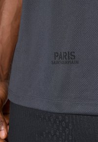 Czarna szara koszulka sportowa z teksturowanego materiału, z napisem "PARIS SAINT-GERMAIN" wydrukowanym na dolnej części.