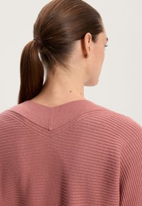 Dusty rose-colored sweater with ribbed texture and a V-shaped neckline. The back shows a smooth finish with subtle stitching details.